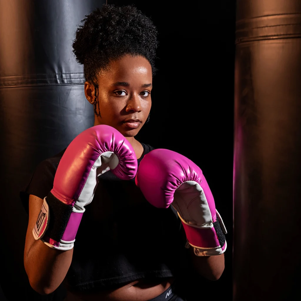 Woman stands with pink boxing gloves.